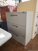Front view of gray metal file cabinet showing three drawers and recessed handles