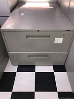 Front view of gray metal 2-drawer filing cabinet showing handles and minor surface wear