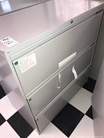 Front view of metal filing cabinet showing three drawers and locking mechanism area.