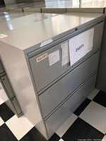 Front and side view of the metal filing cabinet showing three drawers and labels on the top drawer.