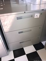 Front view of grey metal filing cabinet with 3 drawers and key lock on top drawer
