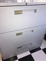 Front view showing three drawers with rectangular handle cutouts and some surface scratches on white metal.