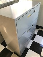 Angled side view of the metal filing cabinet showing three drawers and smooth light gray finish.