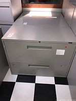 Front view of the gray metal filing cabinet showing 2 drawers with recessed handles and stickers.