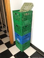 Stacked four plastic milk crates, three green and one blue, in corner near door.