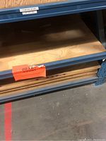 Stack of plywood sheets on blue metal shelving with sign indicating to count the sheets.