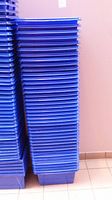 Side view of a tall stack of blue plastic recycling bins lined up against a wall