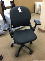 Front view of the black cloth upholstered office chair with vinyl armrests, caster wheels, and adjustable height mechanism.
