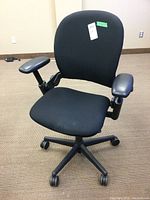 Front view of the black adjustable office chair with cloth upholstery and vinyl armrests on caster wheels.