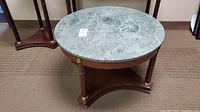 Front top view of round wood table with green marble top showing natural veining and scratches.