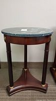 Front view of the wood side table showing green marble round top, three legs and triangular base with brass accents