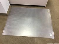 Top view of one clear plastic chair mat showing rectangular shape and some surface reflection.