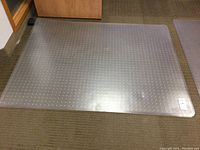 Clear plastic chair mat placed on carpeted floor, showing full rectangular shape and dotted texture.
