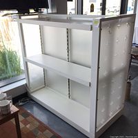 Front and side view of white display case with plus-shaped decorative designs on side panels, two shelves, and open back.