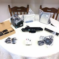 Overview of lot contents on a white tablecloth including Xbox 360 Kinect sensor, cables, receipt printer, chargers and accessories