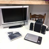 Lot items on table: Insignia 19 inch TV, speaker system, D-Link router in plastic bag, and portable scanner