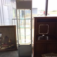 Full front view of tall glass display case with 4 round glass shelves and metal central support pole. Cabinet has glass sides and front with a lockable door at the bottom.