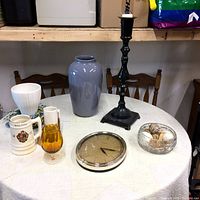Full view of all six home decor items on a round white table, including clock, vases, candle holder, beer mug, and decorative bowl
