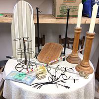 Shows all items on table including wooden candle holders with white candles, ironing board, mop, horse head bookends, metal candle holder and decorative branch sculpture.