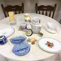 Overview of the table with all household items including plates, vases, candle, gravy boat, glass, and small decor pieces.