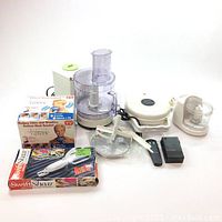 Full view of lot showing 2 food processors, waffle maker, Swift Shear scissors box, and miscellaneous items laid out on white background.