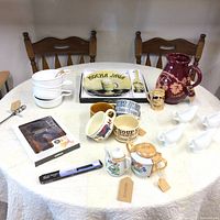 Full view of all items on a round table including cheese cutter, soup bowls, tray, Sangria pitcher, gravy boats, small container, sugar and creamer set, and Craftsman kitchen knife.
