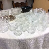 View of all clear glass tea cups, bowls and trays arranged on a table showing the variety of glassware included.