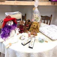 Collection of plush toys, gift basket, bracelets, cushion, blanket, small glasses, and a ceramic container on table.