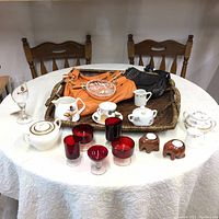 Overall view of lot items on table including two handbags on wicker tray, assorted glassware, porcelain pieces, and elephant candle holders