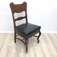 Front right angled view of vintage dining chair showing carved wooden back, leather seat, and front cabriole legs with wheels.
