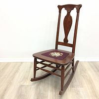 Front view of the wooden rocking chair with visible floral embroidery on seat, showing condition and design