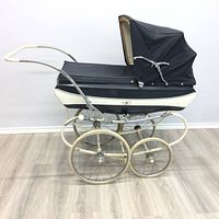 Side profile showing the entire pram with black and cream body, metal frame, and four wheels.