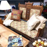 Full view of vintage loveseat showing floral upholstery, wooden arms, and carved wood details with pillows for scale.