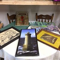Full view of the collection displayed on a round table: lighthouse print, deer photo, Beefeater mirror, charcoal portrait, and a painting.