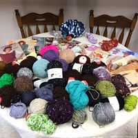 Wide angle of assorted yarn balls in multiple colors and soft textures with knitting pattern books in background.