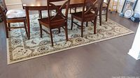 Area rug placed under dining table with wooden chairs on top, showing overall pattern and condition including table leg indentations.