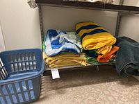 Folded beach towels stacked on metal shelf with laundry basket nearby.