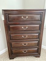 Front view of the five drawer wooden dresser showing dark brown finish and metal handles.