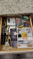 Full drawer view showing assorted tools, small remotes, and hardware in plastic compartments
