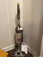 Full view of the Hoover Air Steer upright vacuum cleaner with owner's manual leaning against the wall.