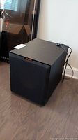 Front and top view of Klipsch R-10SW black subwoofer showing black cloth grille and power cable on top.