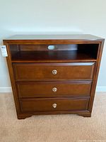 Front view showing three drawers and open shelf with cable hole