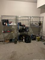 Front view of three assembled metal wire shelving units against a garage wall, with miscellaneous items on shelves.