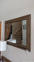 Mirror hanging on wall with natural wood frame visible, reflecting staircase and furniture nearby.