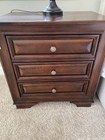 Front view of one nightstand showing three raised-panel drawers with metal knobs.