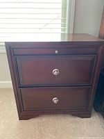 Front view of one nightstand showing two drawers closed and pull-out shelf compartment