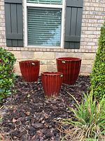 Three reddish glazed clay pots arranged outdoors on brown mulch, showing ridged exterior texture.