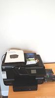 Overview of the HP Officejet Pro 8600 printer with manual, ink cartridges, and photo paper on top and beside the printer.