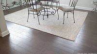 Full view of the area rug under dining table in sunroom-sized space showing size and neutral tone coarse weave pattern.