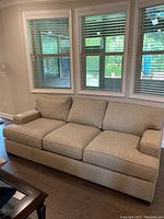 Front view of three-seat beige tweed sofa positioned under three windows